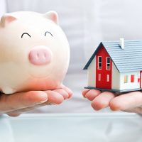 Hands holding a  piggy bank and a house model